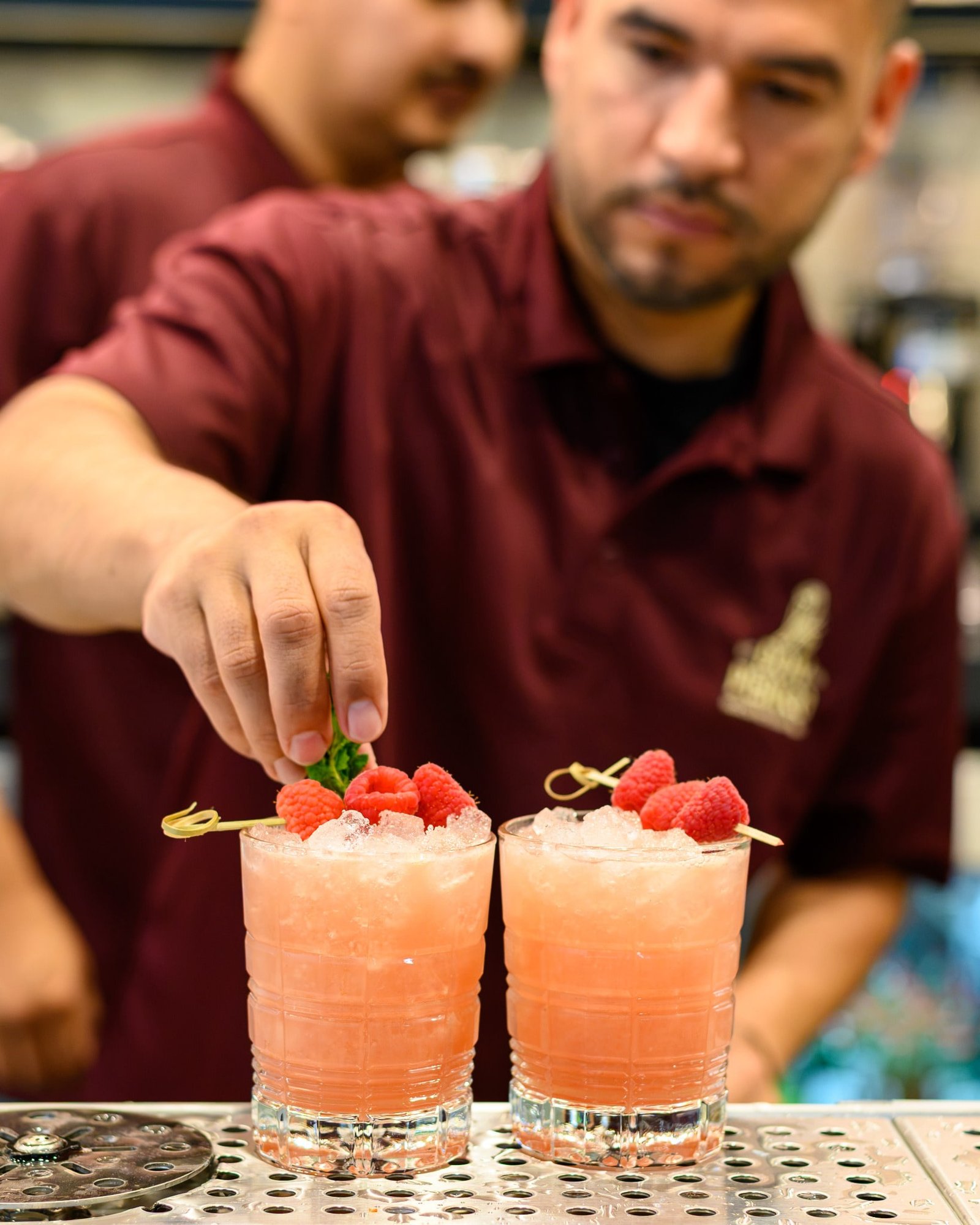 A bartender garnishing two raspberry cocktails