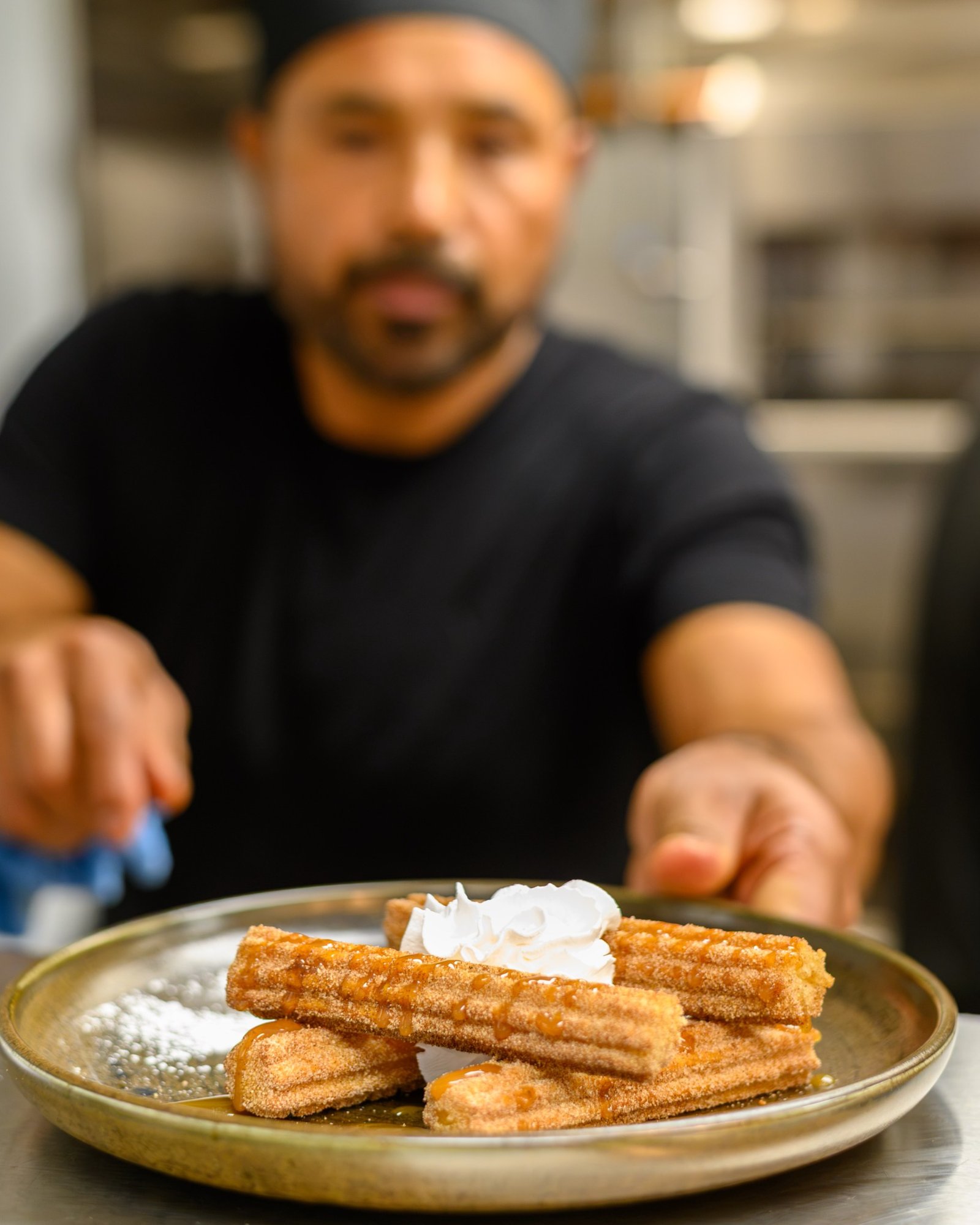A Don Perico team member presenting a finished plate of churros with caramel and whipped cream